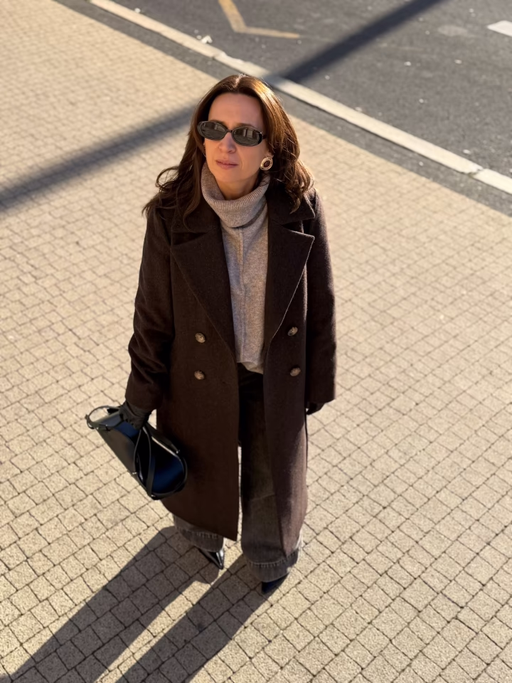 Strona Główna Osobista stylistka w klasycznej, jesiennej stylizacji. Ania Śmiechowska ma na sobie długi, brązowy płaszcz dwurzędowy, szary golf, szerokie jeansy oraz eleganckie, czarne dodatki skórzane.